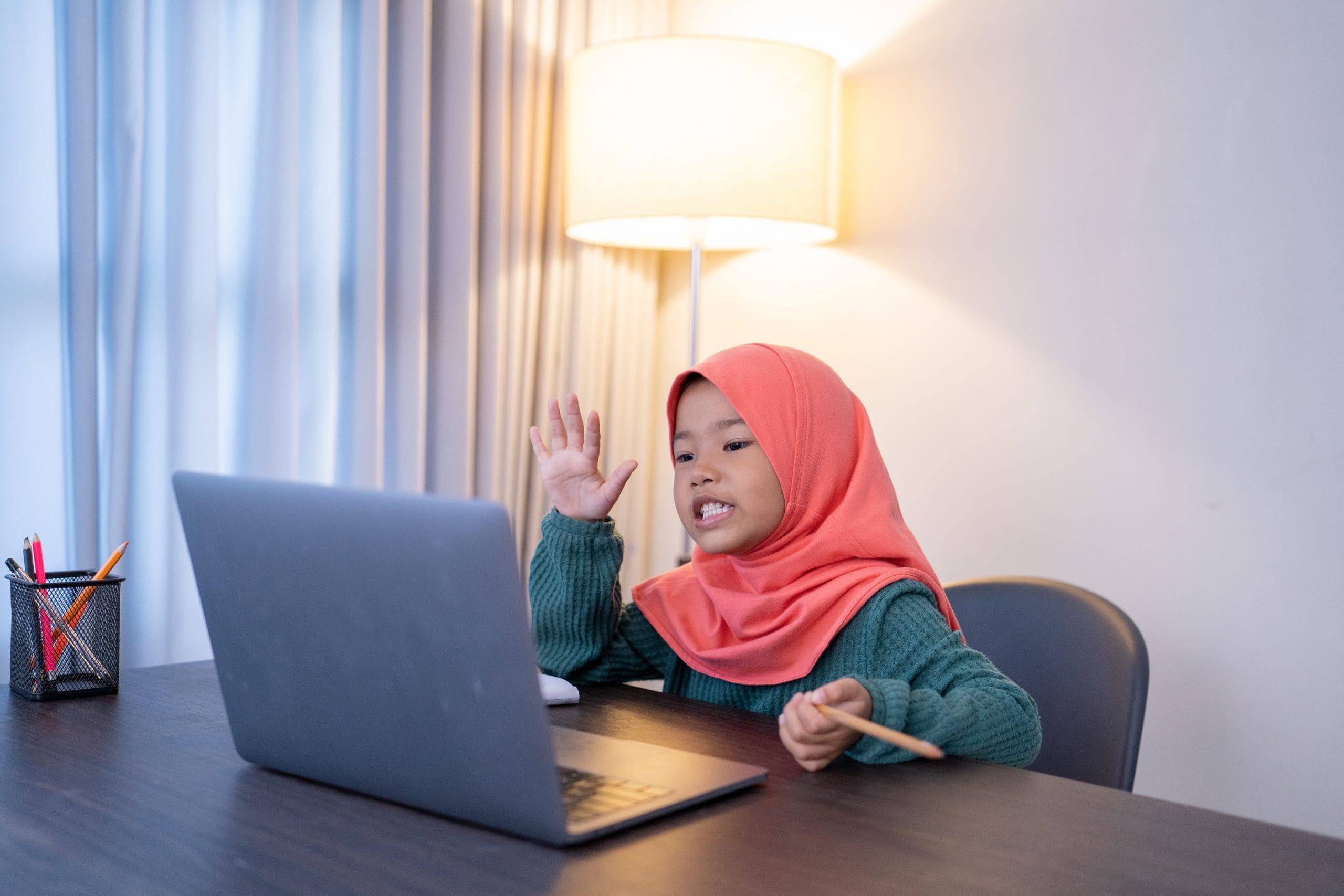 asian muslim elementary student greet her friend and teacher during online class confrerence